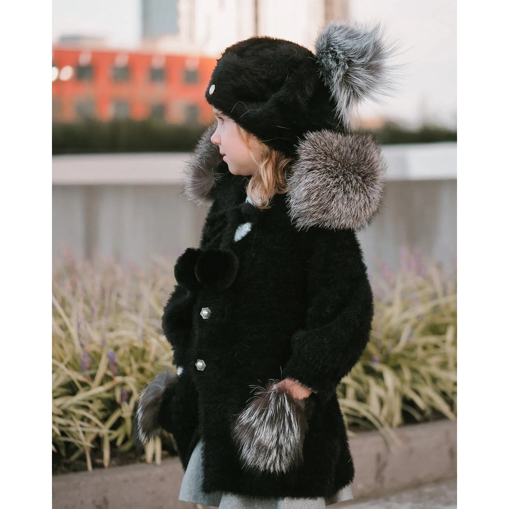 Petite Maison Kids Milana Noir sweater coat, black faux fur with gray fur trim hood and cuffs, worn by a child outdoors.