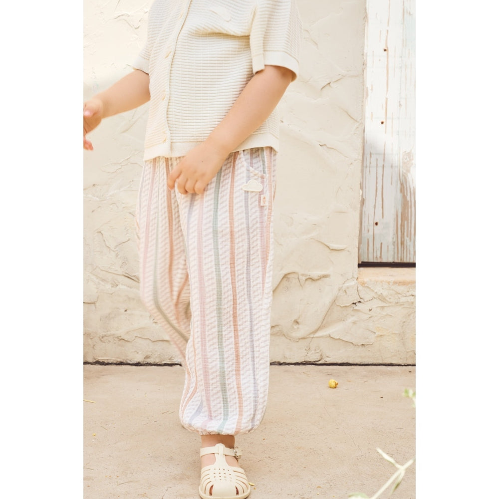 Person wearing a white outfit with striped pants against a stone wall.
