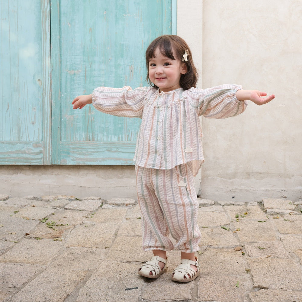 Child in a striped outfit standing on a stone path with a light blue door in the background