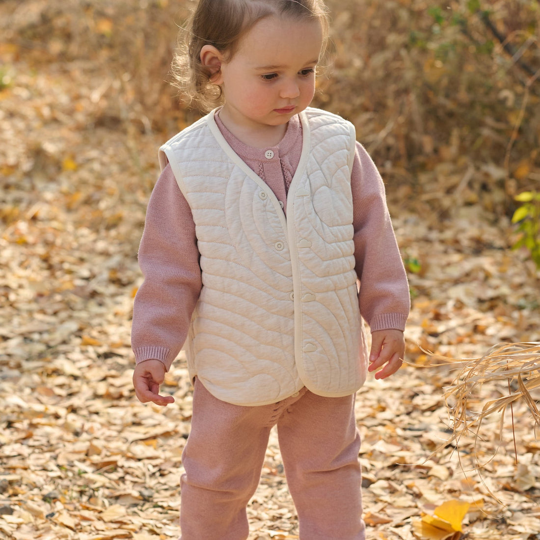 Petite Revery Old Rose Cloud reversible quilted vest worn cream-side out by a child among autumn leaves