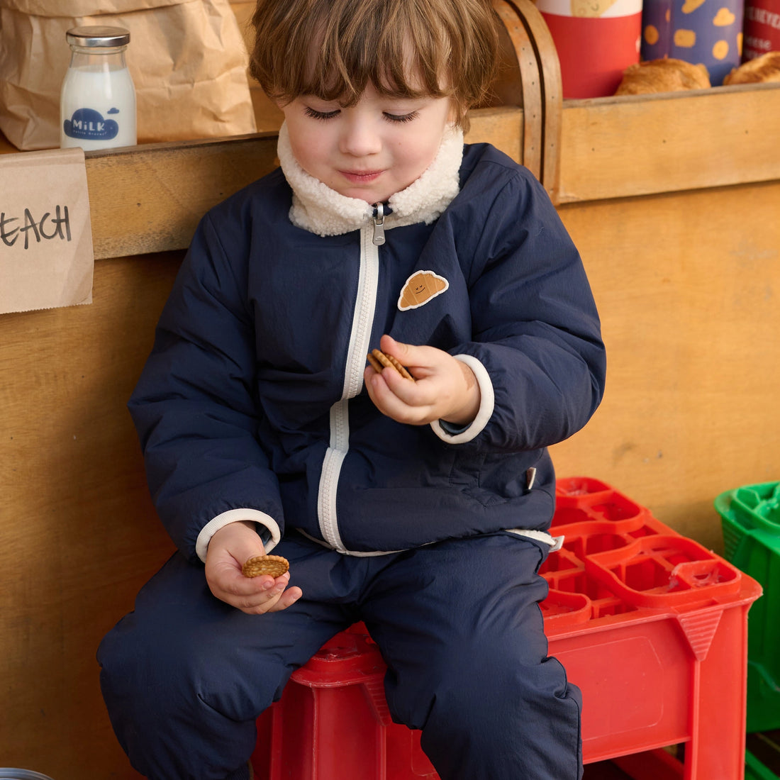 Petite Revery Cozy Crumbs Reversible Fleece Jacket in Blueberry, child wearing the navy side at a market