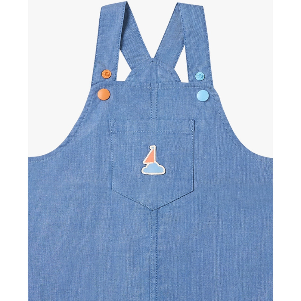 Petite Revery Denim Dress Overalls Sky blue with front pocket and sailboat patch; straps fastened with orange and blue buttons.