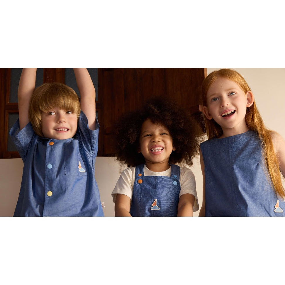 Petite Revery Denim Dress Overalls Sky: three kids in blue denim overalls pose with arms raised.
