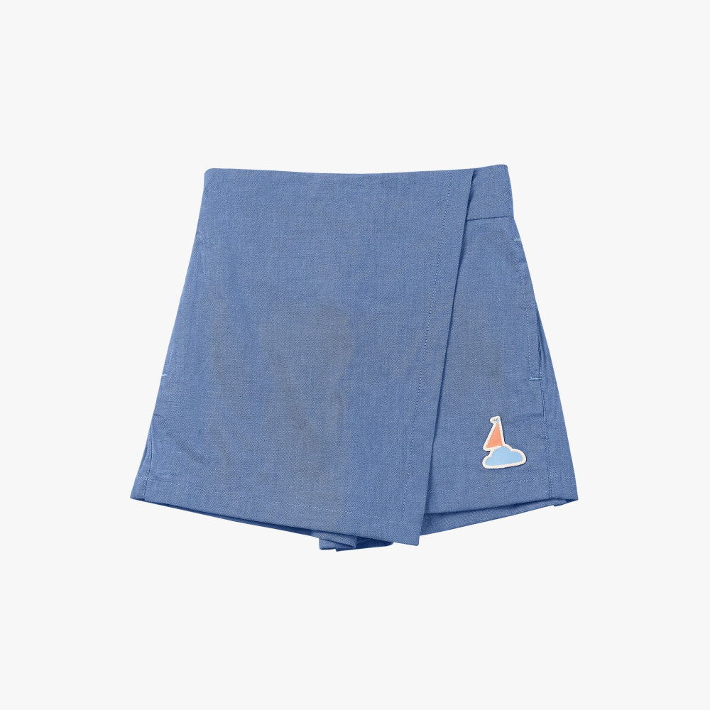 Petite Revery Denim Skort Sky in blue chambray, laid flat to reveal the sailboat patch logo.