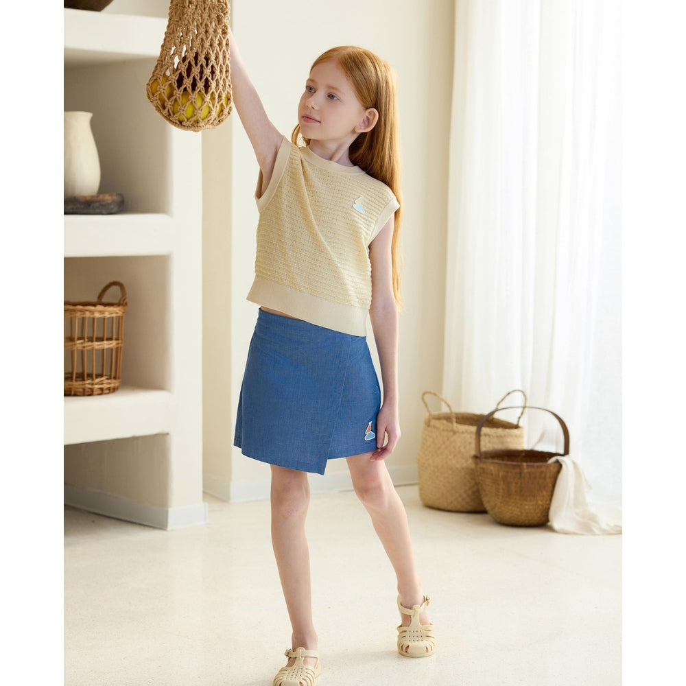 Petite Revery Denim Skort Sky in blue denim; girl stands reaching up, showing knee-length skort and casual sandals.