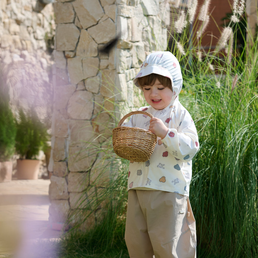 Child in a garden holding a basket, standing next to a stone wall.