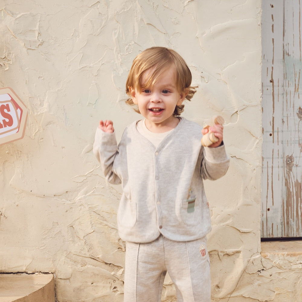 Child in a gray outfit standing against a textured wall.