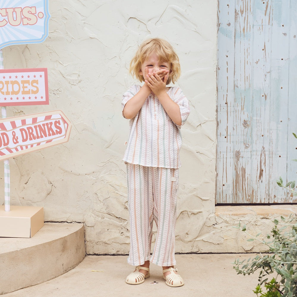 Child in striped outfit standing in front of a rustic wooden door with decorative signs.