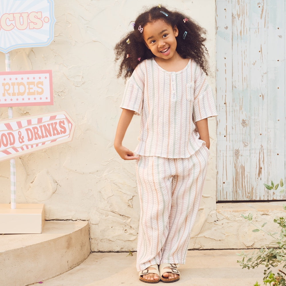 Young girl in a striped outfit standing outdoors with decorative signs in the background