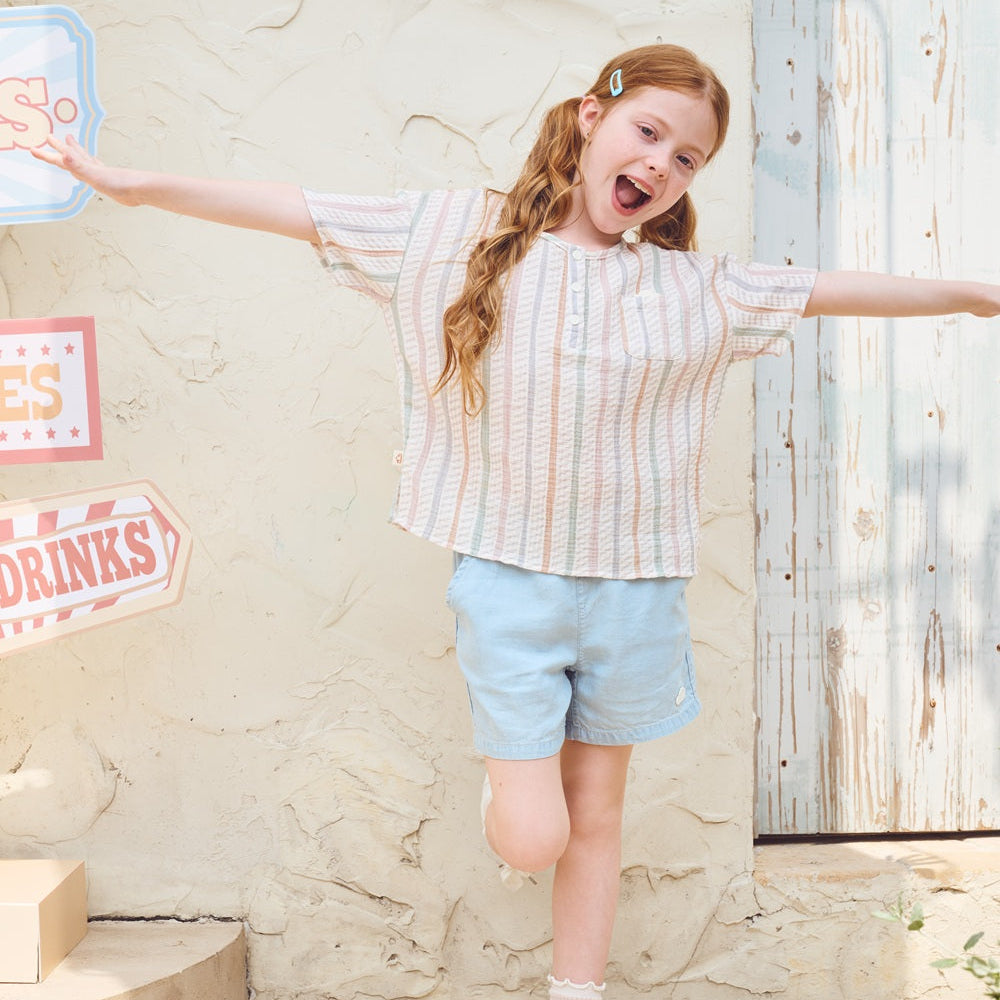 Young girl with arms outstretched in front of a stone wall with signs.