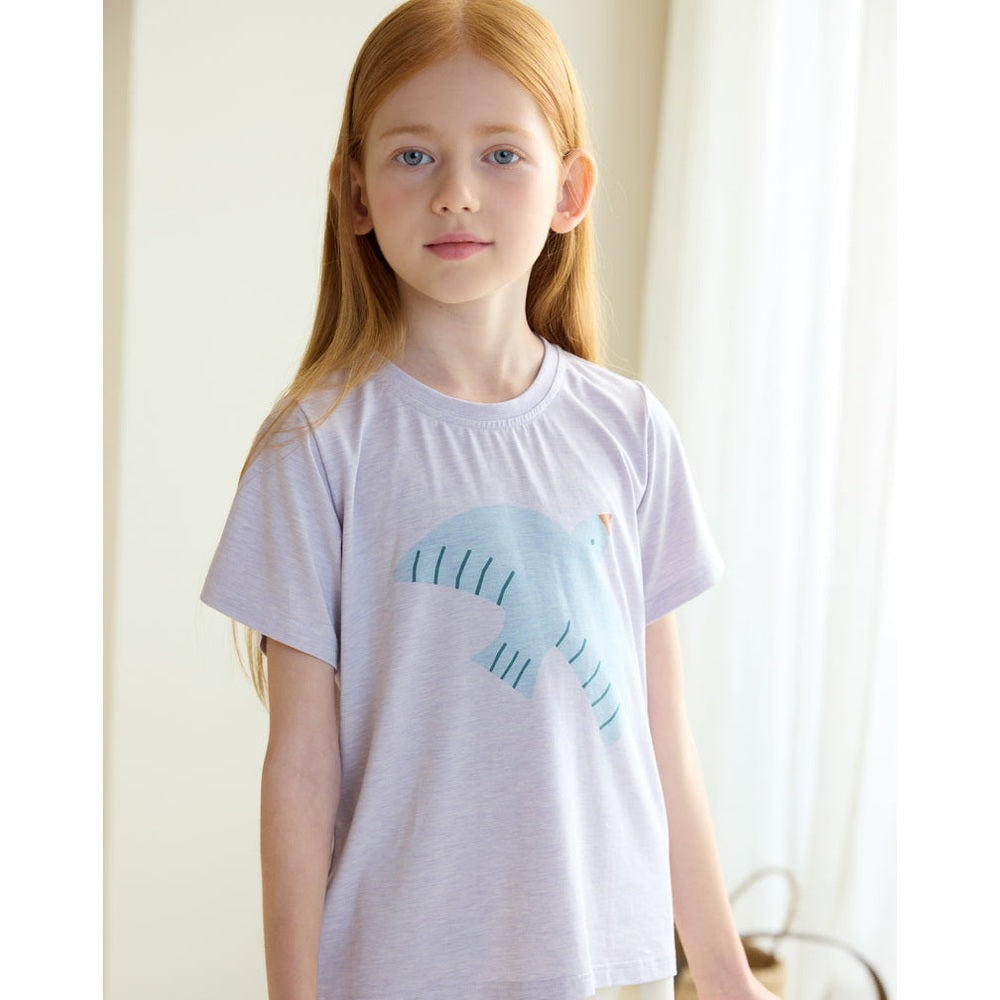 Petite Revery Short Sleeve Tee Lavender Blue worn by a girl, displaying a teal dinosaur graphic.