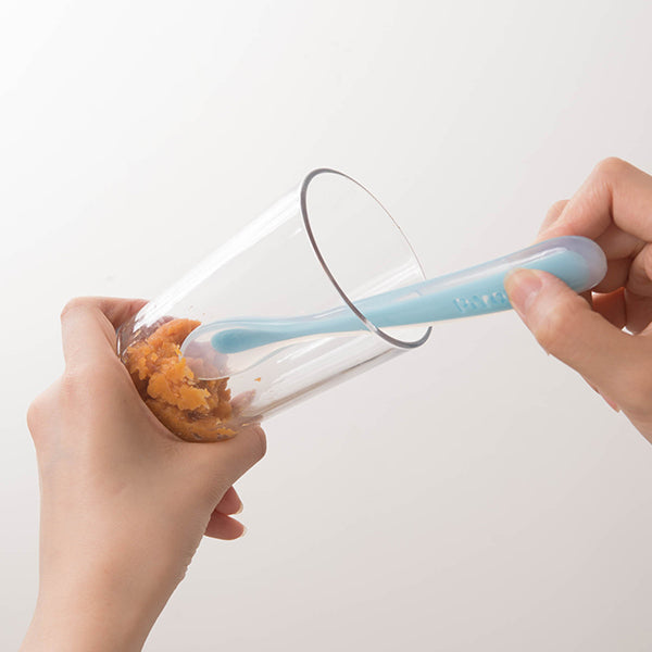 PIYO PIYO silicone baby feeding spoon in blue, shown scooping orange puree.