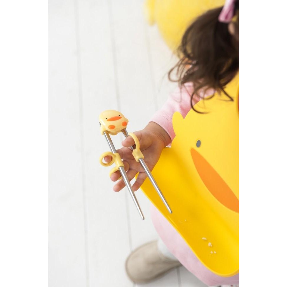 Piyo Piyo Stainless Steel Training Chopsticks with duck topper, gripped by a child wearing a yellow bib