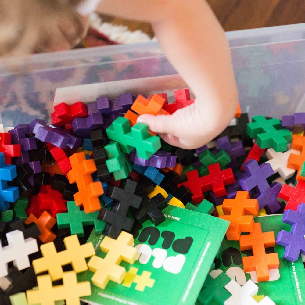 Plus-Plus Big 400 Educational building toy set in multicolor cross blocks; child reaches into the pile to pick pieces.