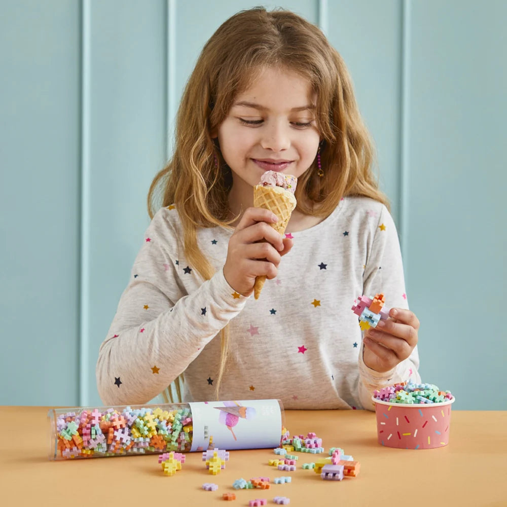 Child building with PLUS PLUS pastel pieces while enjoying ice cream, showing the Mix 240 Pieces Tube and small creations made from the interlocking blocks