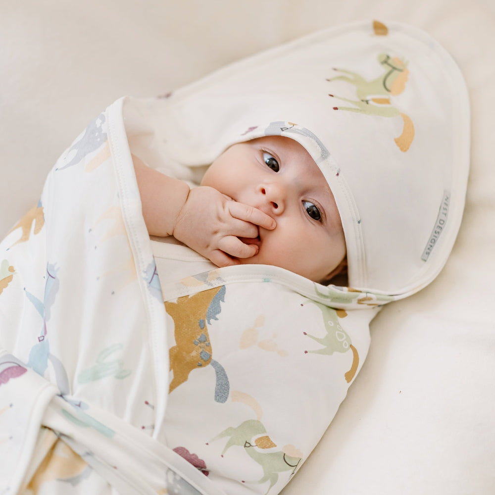 Baby wrapped in a colorful blanket with a hood on a soft surface