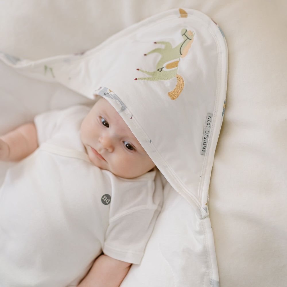 Baby wrapped in a white blanket with cartoon deer design, lying on a soft beige surface.