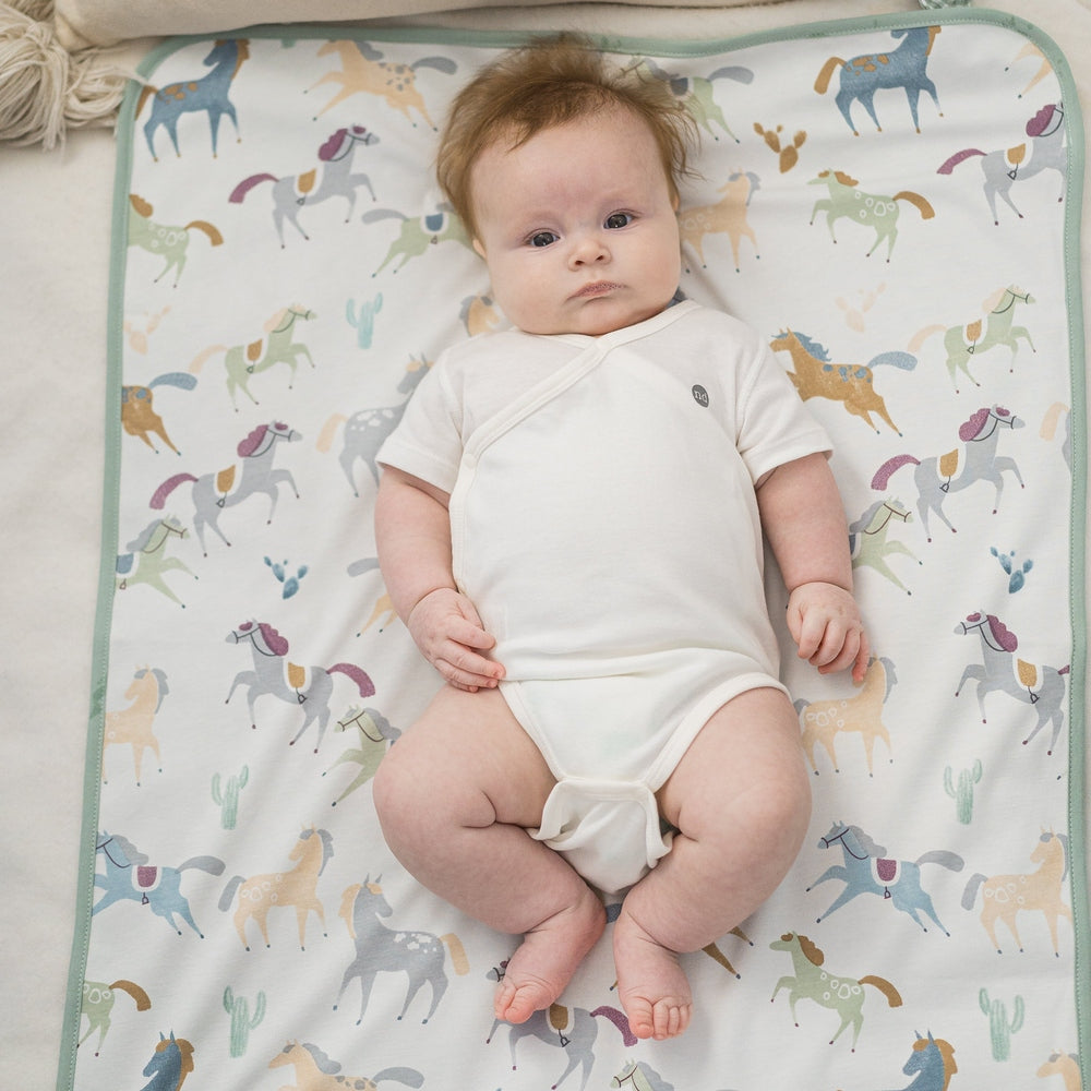 Nest Designs Pony Express Collector's Bundle in white onesie on a horse-print blanket with mint trim.