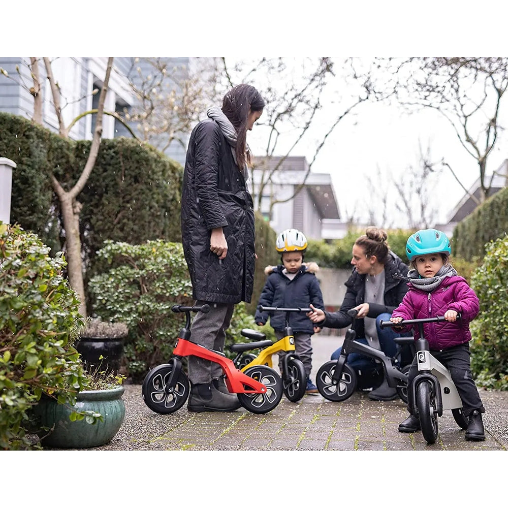 Qplay Balance Bike: four kids ride red, yellow, gray and black bikes while adults supervise in a garden.