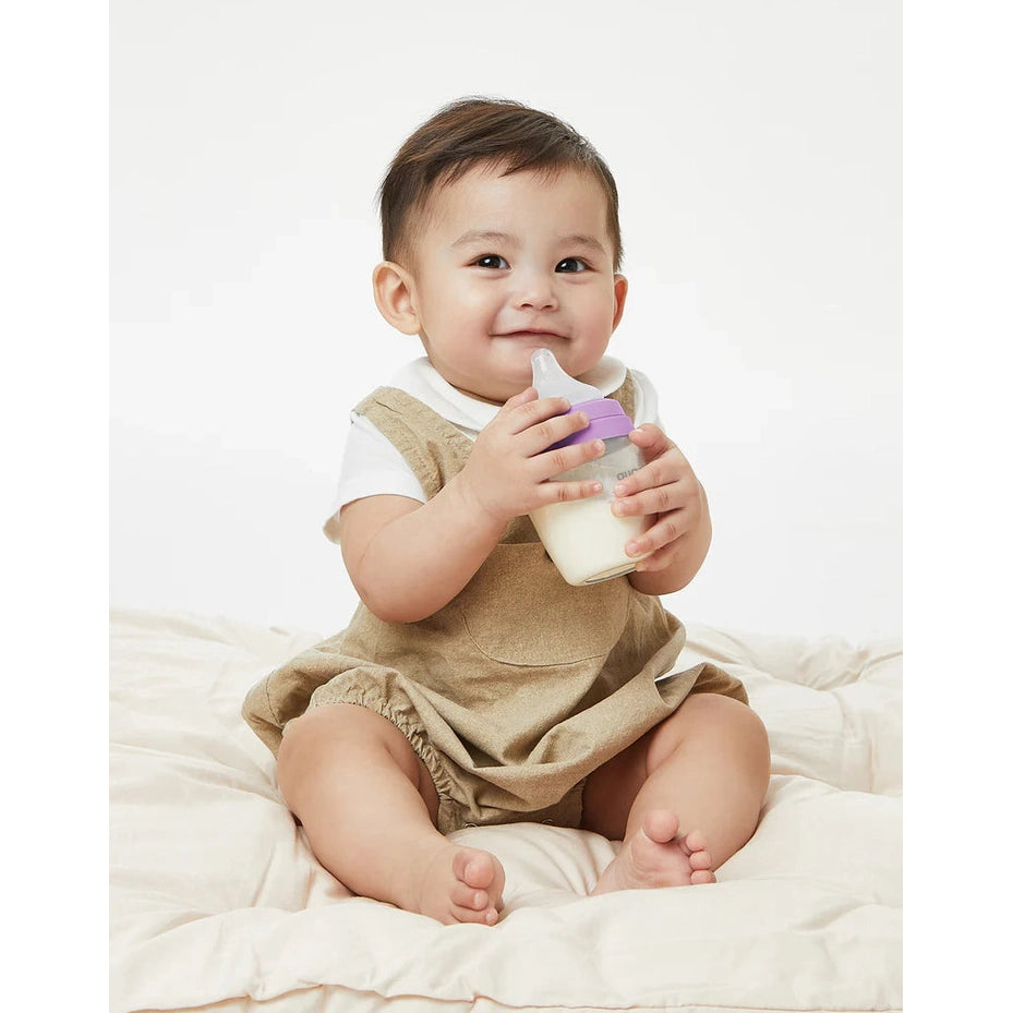 Quark Buubibottle Mini Hybrid Feeding Bottle held by a smiling baby, showing the purple-lid transparent bottle.