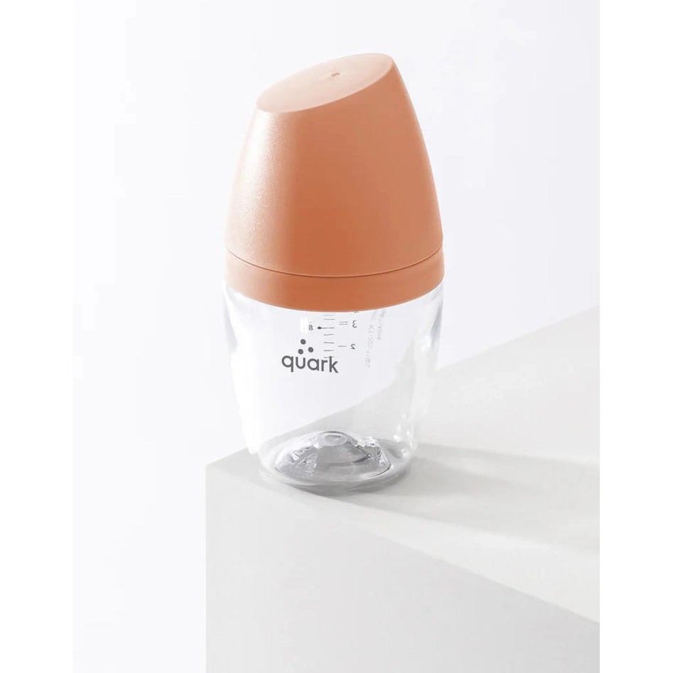 Quark Buubibottle Mini Hybrid Feeding Bottle 1 Pack with peach cap and clear, measured body, standing on a white surface.