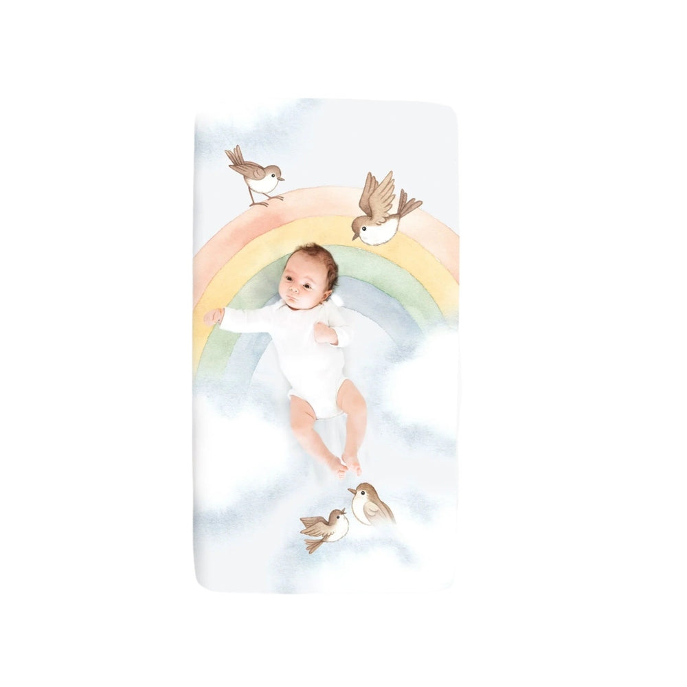 Rookie Humans cotton sateen crib sheet featuring a pastel rainbow and birds with a baby on it