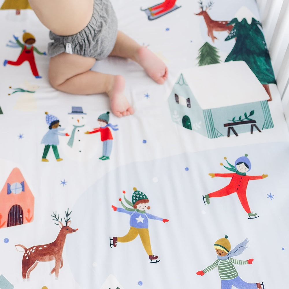 Rookie Humans crib sheet in cotton sateen with snowy day winter illustrations of kids ice skating and houses