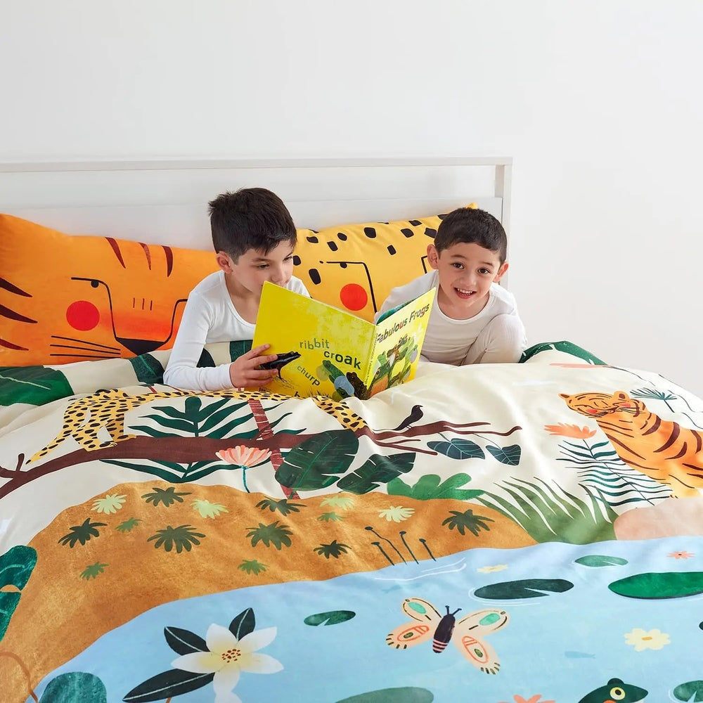 Rookie Humans Kids Bedding Set In The Jungle with bright tiger and foliage print as two kids read on the colorful bed.