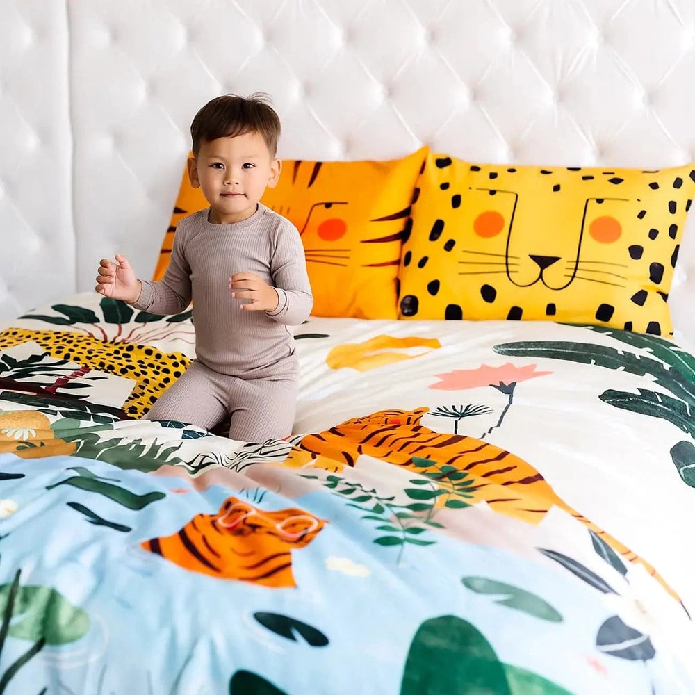 Rookie Humans Kids Bedding Set In The Jungle: child sits on jungle-print comforter with yellow animal-face pillows.