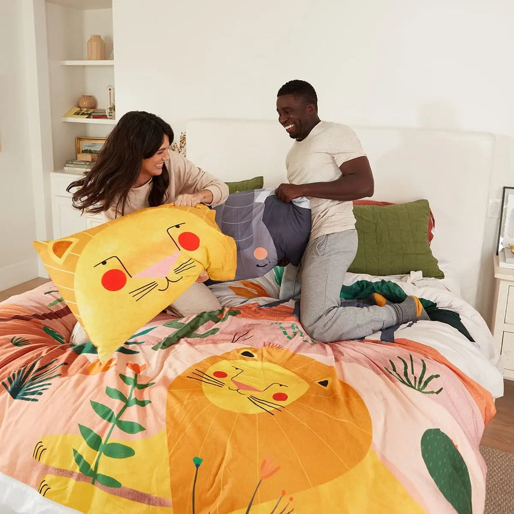 Rookie Humans Kids Bedding Set In The Savanna on a bright bed, where a couple tosses the lion-print duvet and matching pillow covers.