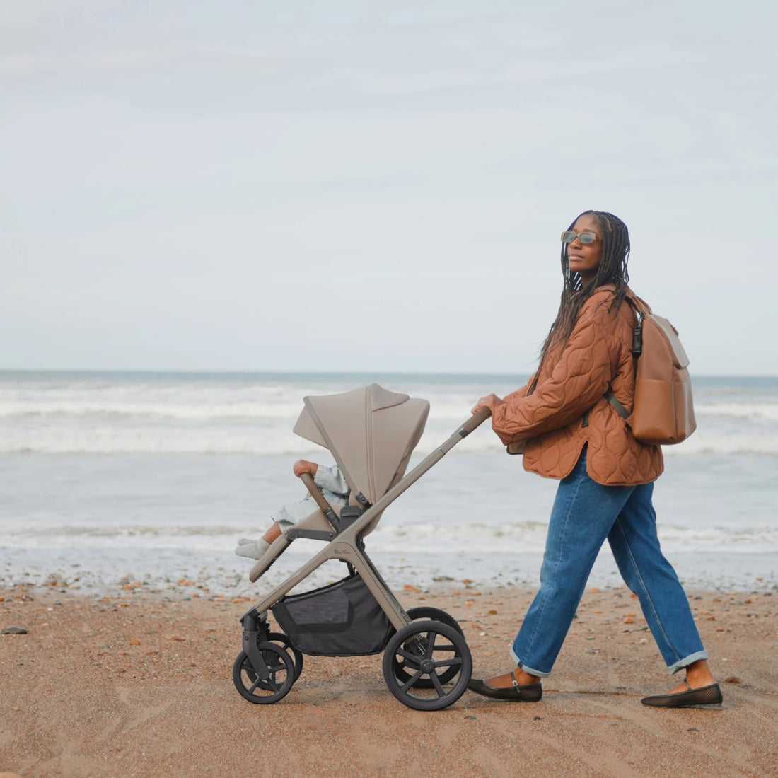 Parent walking beside the sea with the Champagne Cove 2 stroller in a forward-facing seat configuration.