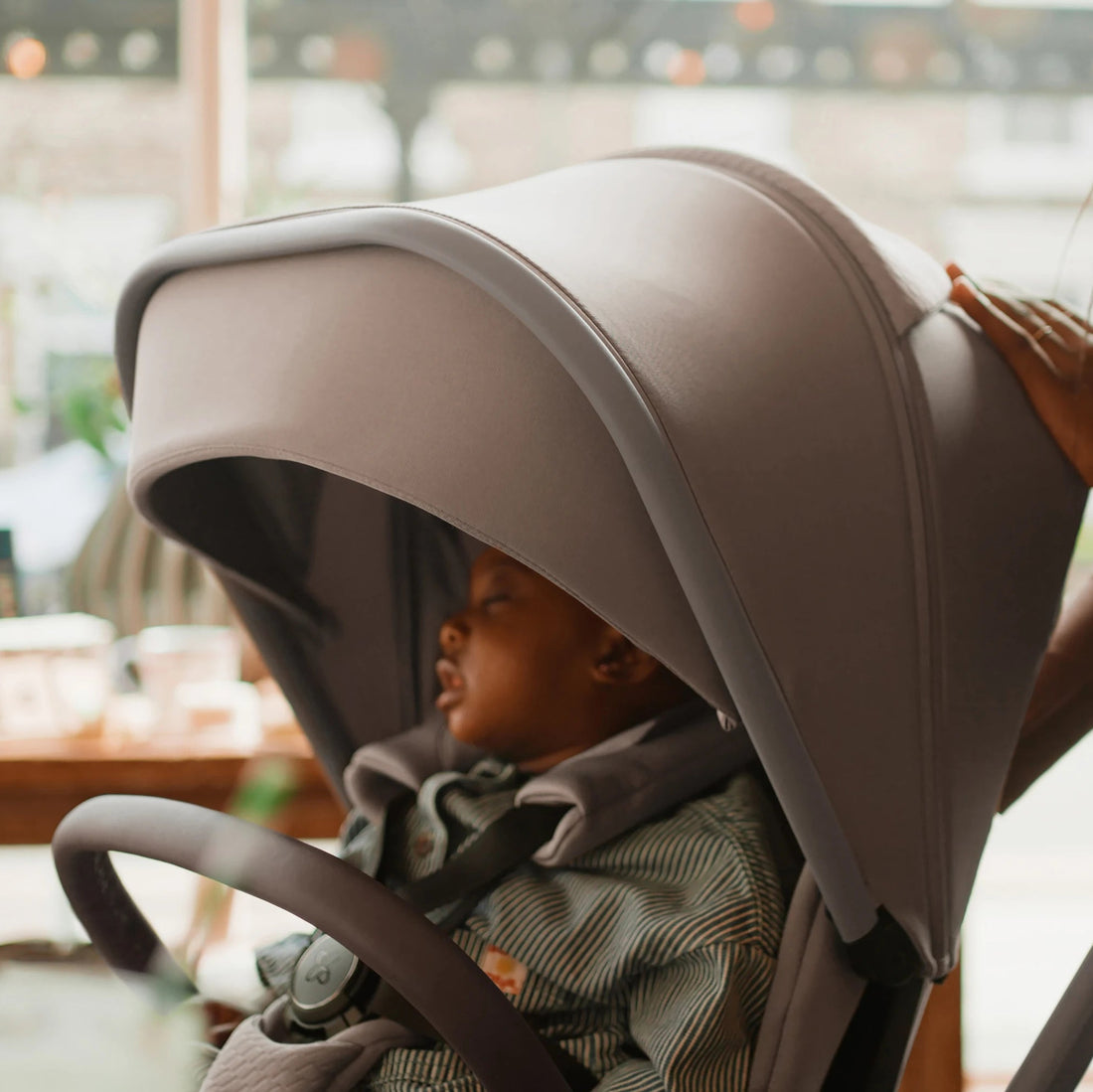 Child seated beneath the Champagne Cove 2 stroller canopy in a café.