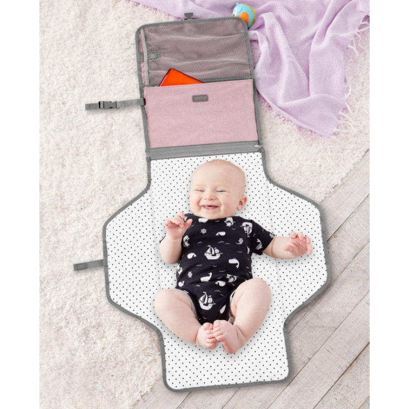 Skip Hop Pronto Signature Changing Station Pink Heather changing mat with gray trim and a baby on a white polka-dot surface