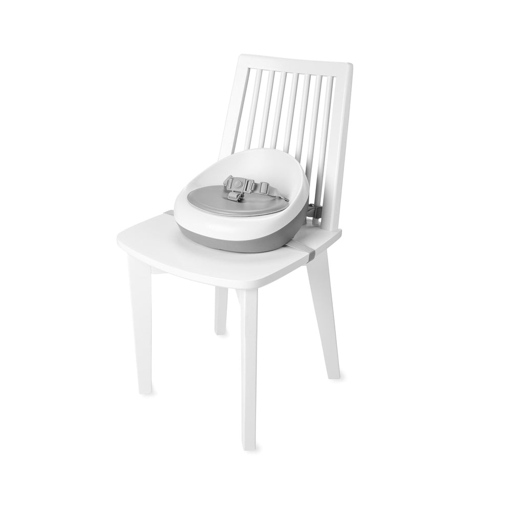 Skip Hop Sleek Seat Booster in grey/white attached to a white chair for feeding