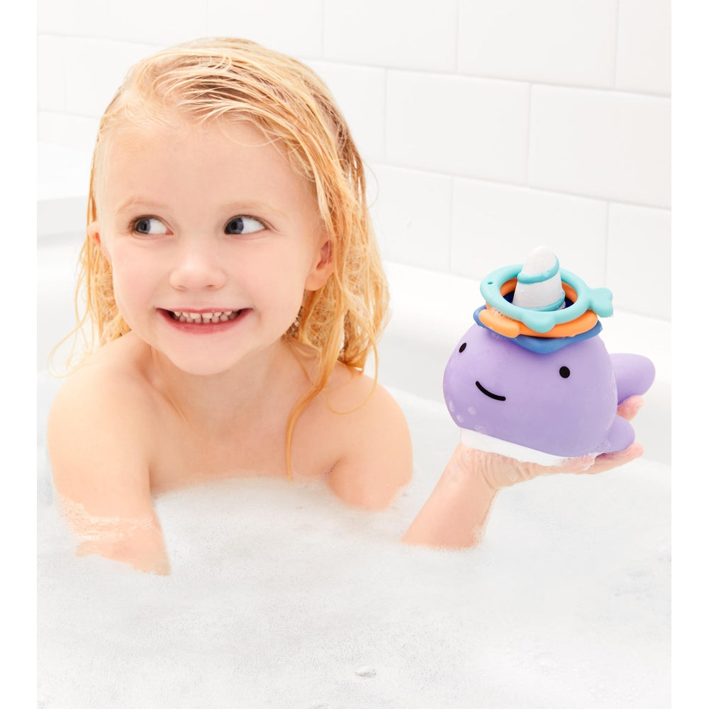 Skip Hop Zoo Narwhal Ring Toss bath toy in purple with colorful rings, held by smiling child
