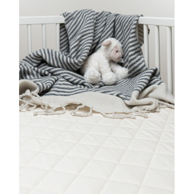 Sleeptek Organic Rubber Crib Mattress in a white crib, wrapped by navy striped blanket with a plush bear