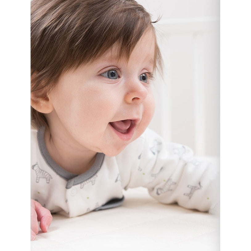 Sleeptek Organic Rubber Crib Mattress; smiling baby reaches across a clean white surface, showcasing cozy safety.