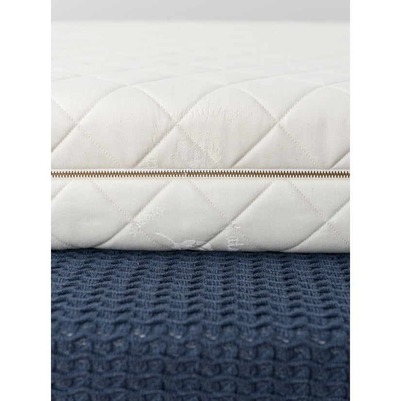Sleeptek Organic Rubber Crib Mattress white quilted cover with zipper along the edge resting on a blue textured surface.