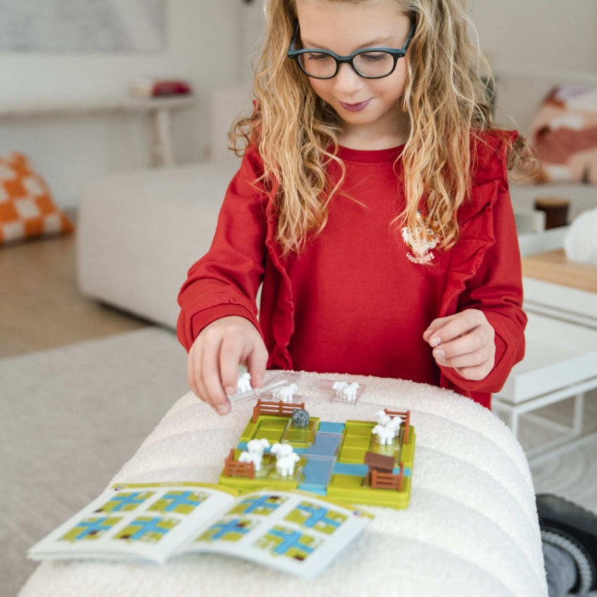 Smart Games Counting Sheep puzzle game; child plays with a colorful grid and white sheep pieces.