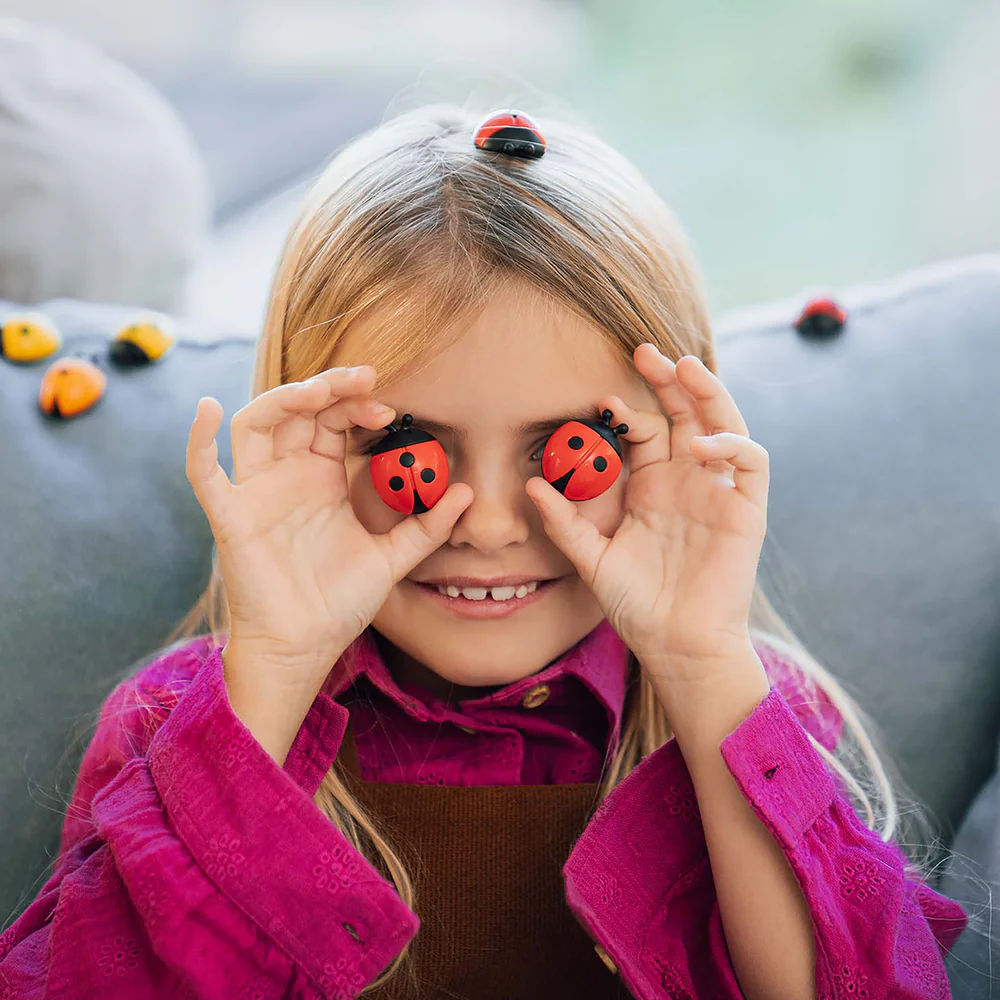 Child holding ladybug-shaped objects over their eyes with a blurred outdoor background