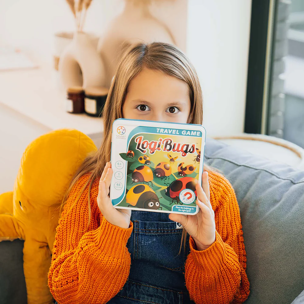 Child holding a 'LogiBugs' travel game box on a couch