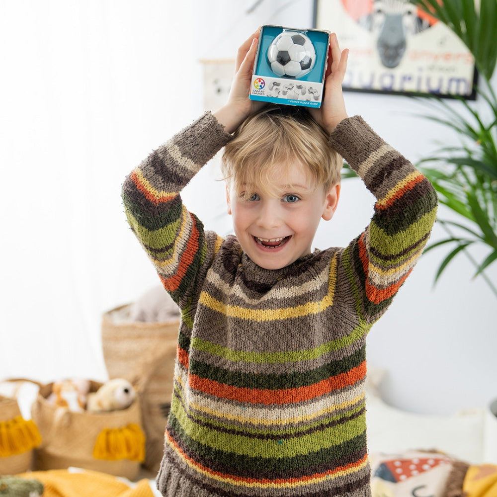 Smart Games Plug & Play Ball box held above head by smiling child in a multicolor striped sweater