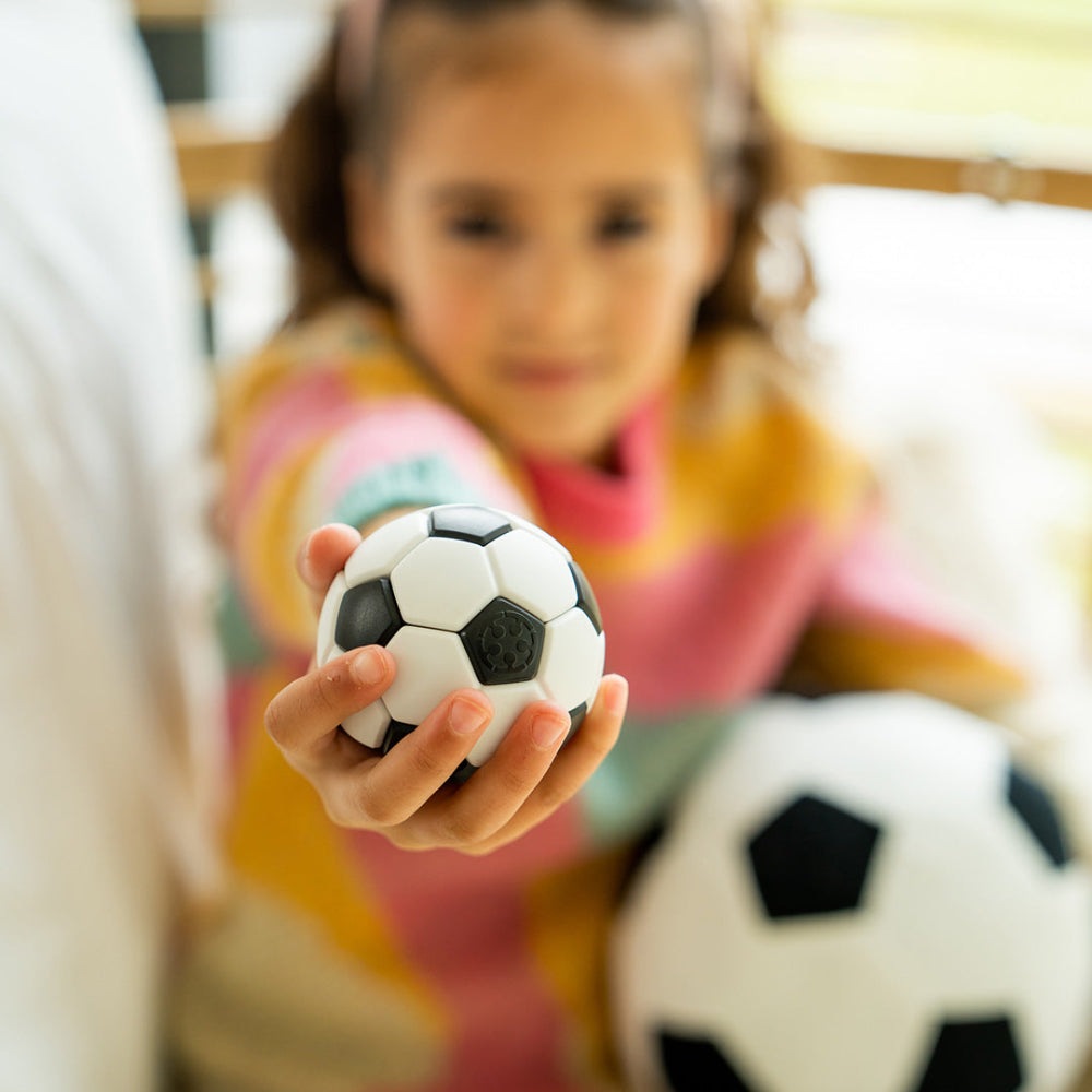 Smart Games Plug & Play Ball held by a child with a full-size black-and-white soccer ball nearby