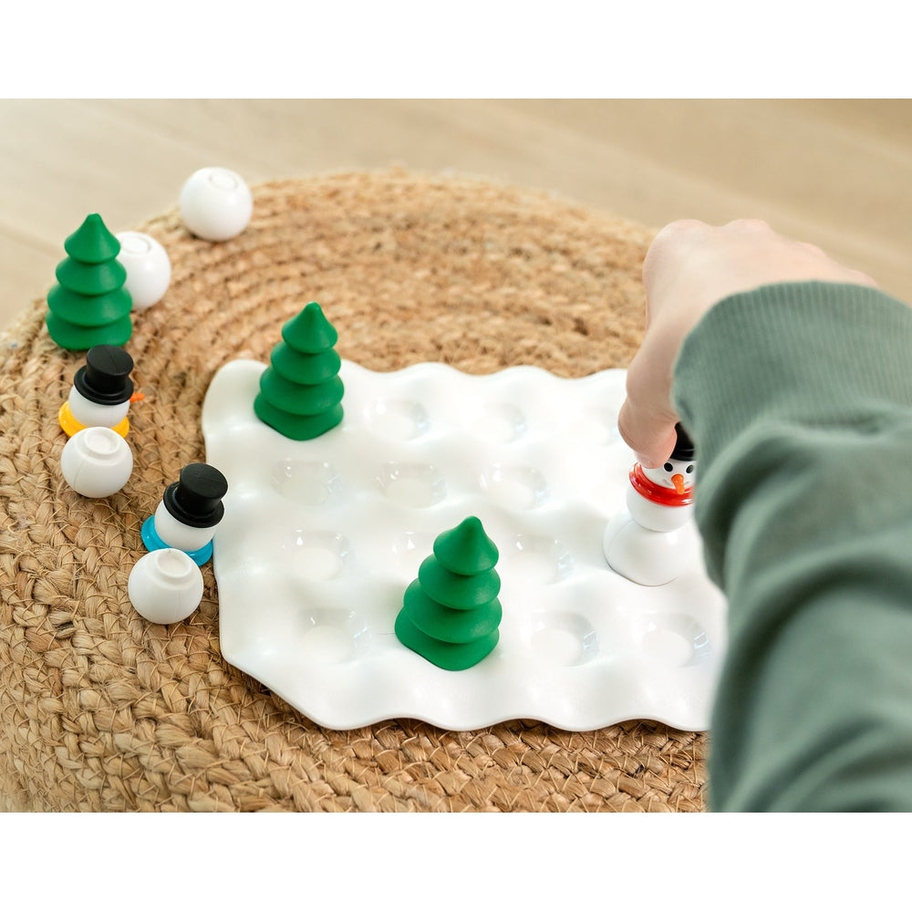 Smart Games Snow Problem puzzle: child places a snowman piece on a white wavy grid with green trees.