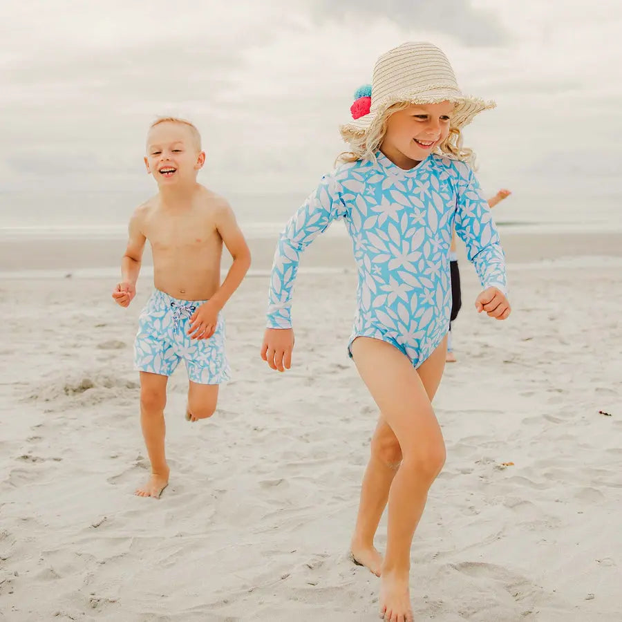 Snapper Rock Aqua Bloom Sustainable LS Surf Suit for kids, blue leaf print; children sprint along sandy beach.