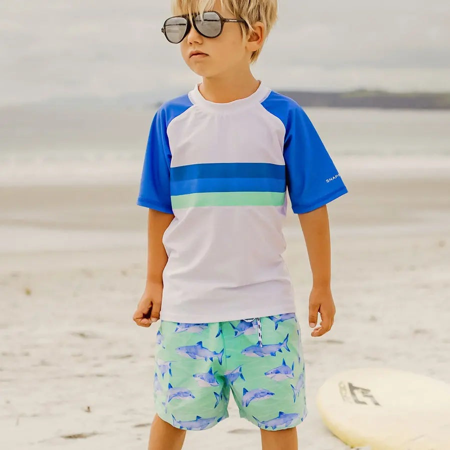Snapper Rock Minty Shark Volley Board Short, mint green with blue shark print, worn by kid on sunny beach.