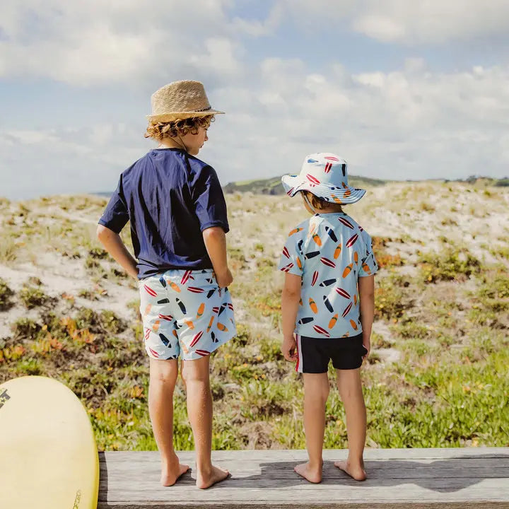 Snapper Rock Retro Surf Baby Set: two toddlers in light-blue swim shirts and shorts with surfboard print, beach boardwalk scene.