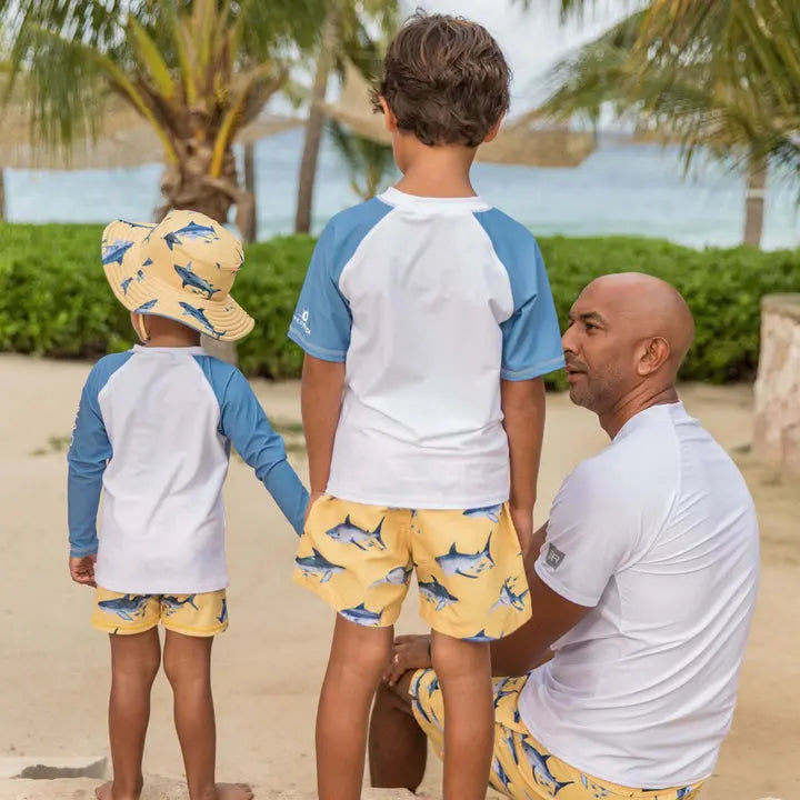 Snapper Rock Sunrise Shark Baby Set; two toddlers in white-blue raglan tops and yellow shark-print shorts on a sunny beach.
