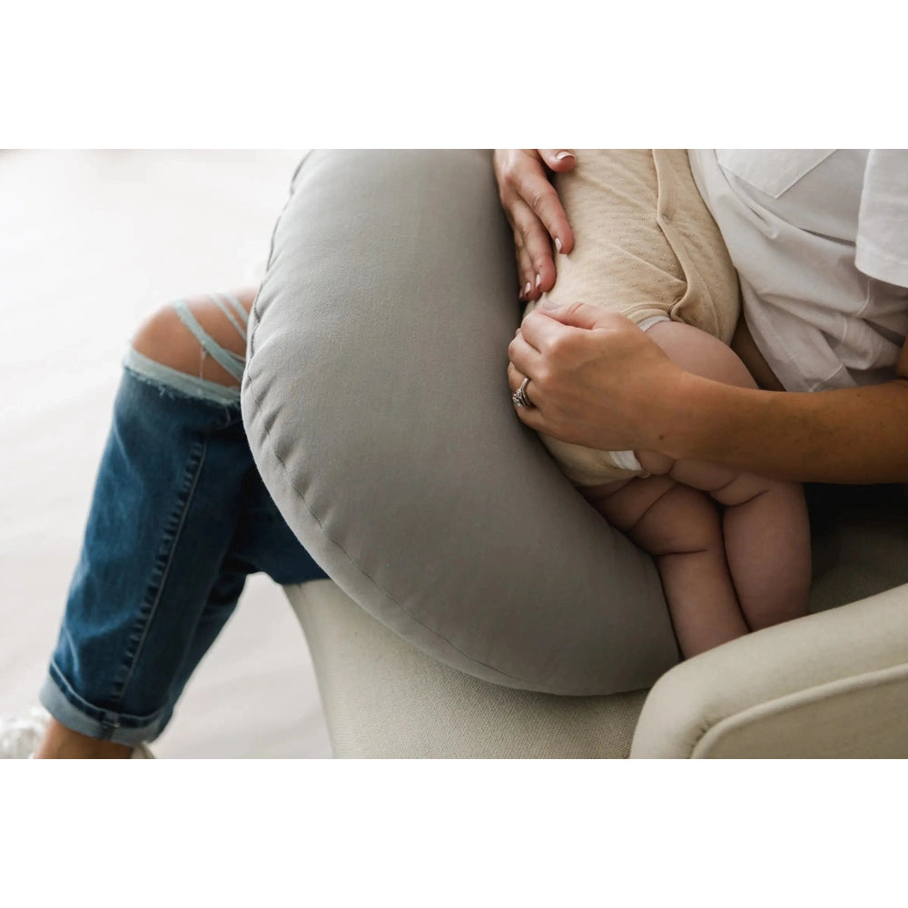 SNUGGLE ME ORGANIC Feeding Support pillow cradles baby as parent holds them securely on a chair.