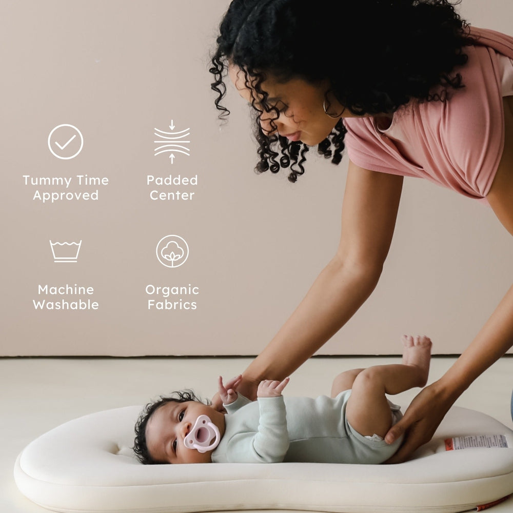 Snuggle Me Organic Lounger Curve: mother places baby on the padded center, showcasing organic fabrics and machine-washable design.